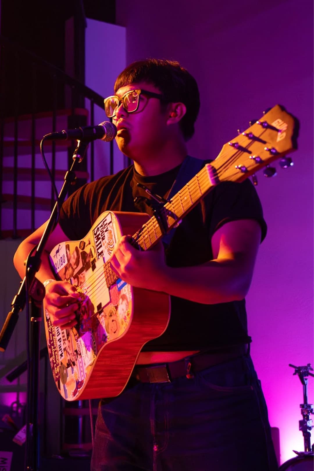 A young performer sings into a microphone under blue stage lighting